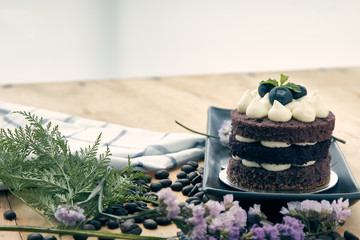 Brown cake with berry on top placing with pink flower as decorated item on the wooden table