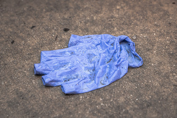 Close up of a used wet blue latex protective or medical glove laying crinkled and wrinkled and partially inside out with water droplets and dirty on the damp sidewalk or pavement.