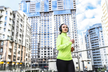 A young woman in sportswear is running with headphones on her head on the street outdoors. Healthy lifestyle concept