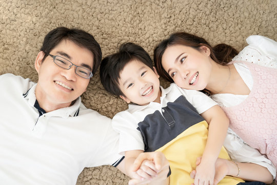 Asian family happy laughing and smiling together lying down on carpet floor, parent and kid is real people family.