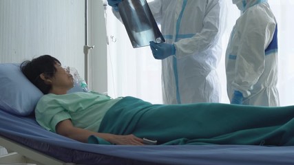 doctor and nurse in personal protective equipment or ppe looking at chest x-ray of the patient who infected with covid-19 or coronavirus in hospital. medical concept - Powered by Adobe