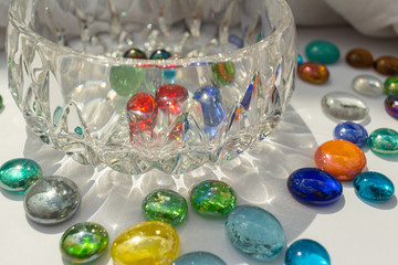 Large modern crystal glass bowl surrounded with multi-color glass drop dragon tears, on white background with copy space