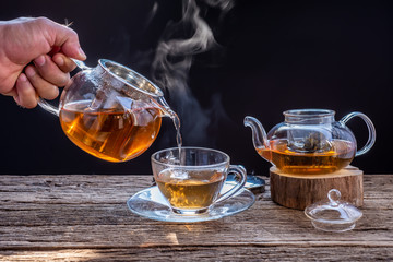 A cup of tea on a wooden table,process brewing tea,Cup of freshly brewed fruit and herbal tea, darker background. .Hot water is poured from the kettle into a cup with tea.