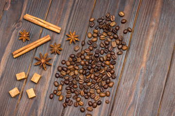 Coffee beans scattered on table, star anise, cinnamon sticks and pieces of brown sugar.