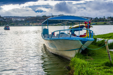 Fototapeta na wymiar IMBABURA, ECUADOR SEPTEMBER 03, 2017: Outdoor view of a boat parket in the Yahuarcocha lake border,with other duck boat parked, in a cloudy day