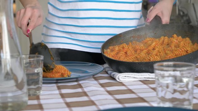 Young woman serving pasta from a pan, close up