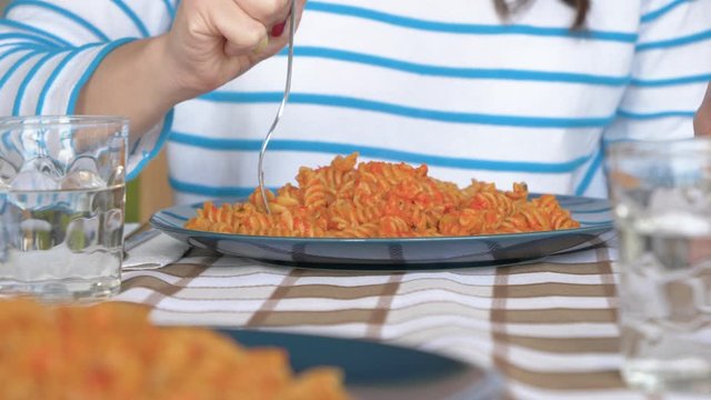Slow motion shot of young woman eating fresh pasta on plate, close up
