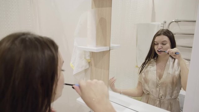 Young brunette girl with long dark hair in bright clothes is washing fun and brushing her teeth at home in the bathroom