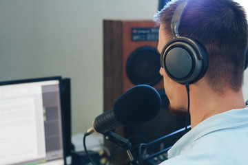A young male radio host with headphones in front of a microphone