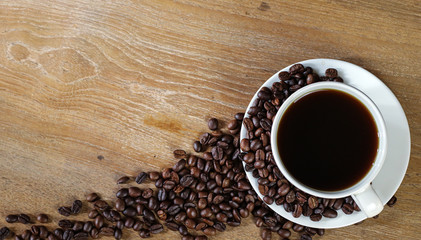 White coffee cup and coffee beans on wooden table with copyspace for text. Selective focus.