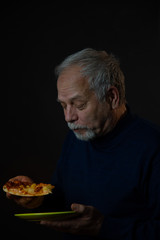 aged person with grey beard and receding hairline eats pizza holding green plate close view. Concept man emotion