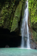 A waterfall falls beside a dark cave, pooling in a clear waterfall vault