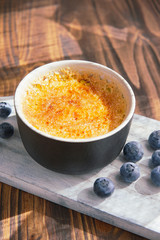 Creme brulee or catalana - traditional French vanilla cream dessert with caramelised sugar, blueberries on rustic white wooden board, table with sunny light. Sweet dessert -custard. Copy space.