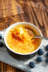 Creme brulee or catalana - traditional French vanilla cream dessert with caramelised sugar, blueberries on rustic white wooden board, table with sunny light. Sweet dessert -custard. Copy space.