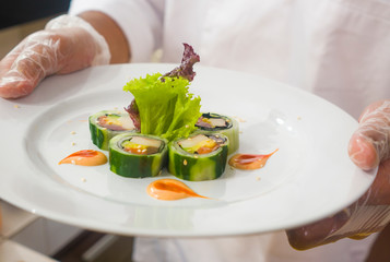 hands in gloves of Asian professional chef preparing delicious and healthy Japanese sushi rolls at restaurant kitchen working with beautiful ingredients making traditional Japan food