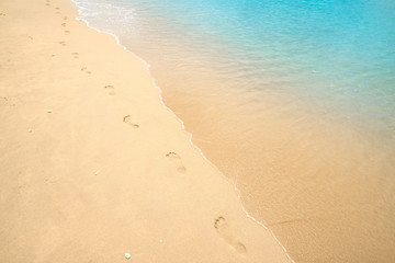 Footprints on sandy beach. Steps of human feet on clear gold sand with water sea line texture....