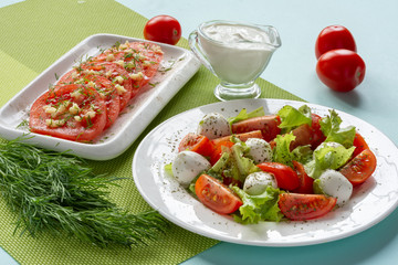 Italian Caprese salad with sliced tomatoes, mozzarella cheese, lettuce leaves, olive oil on a plate. Still-life.