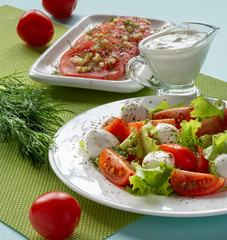 Italian Caprese salad with sliced tomatoes, mozzarella cheese, lettuce leaves, olive oil on a plate. Still-life.