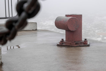 An iron chain on a pier on a cloudy, foggy morning covered in drops of water.