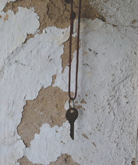 old metal rusty key to the lock hanging on a lace against a clay wall with crumbling whitewash