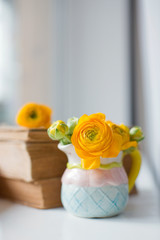 Orange ranunculus in cute small pitcher and stack of vintage books
