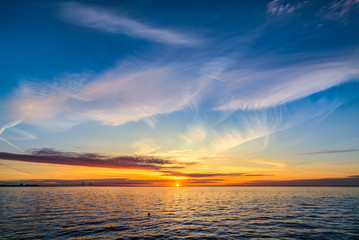Sunset over the Øresund Bridge. Beautiful orange seascape sunset. White cirrus clouds on the pastel colored blue sky. Beautiful reflection in the sea waves.