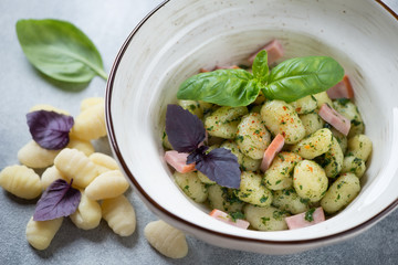 Close-up of potato gnocchi served with basil pesto sauce, chopped bacon and fresh basil leaves, selective focus, studio shot