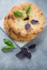 Two ossetian pies on top of each other with red and green basil leaves, elevated view on a light-blue stone background, studio shot