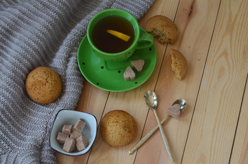 A Cup of lemon tea, a warm sweater, cookies, and heart shaped brown cane sugar on a wooden table. A pleasant tea party in a cozy atmosphere at home
