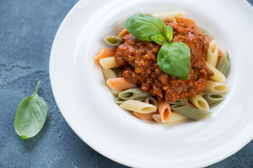 Close-up of italian penne pasta served with bolognese sauce and fresh green basil in a white plate, selective focus
