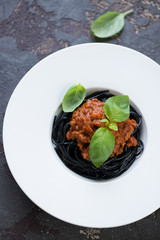 White plate with squid-ink spaghetti and bolognese sauce on a brown stone background, vertical shot, above view