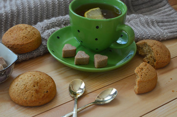 A Cup of lemon tea, a warm sweater, cookies, and heart shaped brown cane sugar on a wooden table. A pleasant tea party in a cozy atmosphere at home