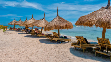 Tourism on Gili Air Island in Indonesia, with a row of thatched sunshades and bamboo furniture for tourists on a white sand beach next to beautiful turquoise water.