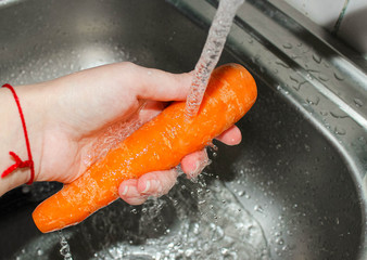 A woman's hand washes carrots under a stream of water.