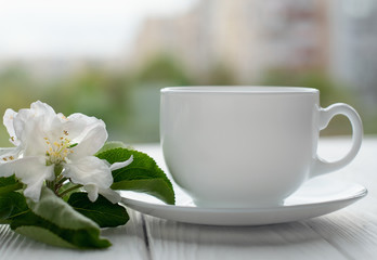 Hot tea in white porcelain cup with white flowers on a branch of apple
on a white wooden background