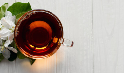 Transparent glass cup with hot tea and a branch of white flowers on a white wooden background