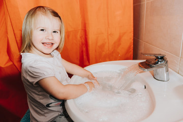 Cute little toddler girl washing her hands in a bathroom. Hygiene concept showing prevention of infection and viruses such as flu and covid-19