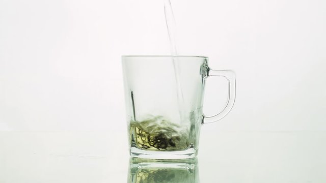 black tea particles pouring into glass transparent mug and adding boiling water to brew tea isolated on white background close up .