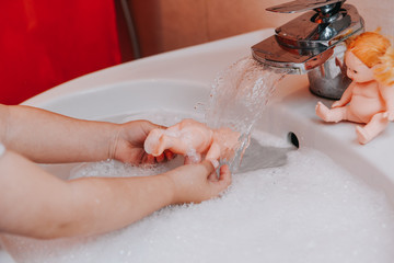 Fototapeta premium Cute little toddler girl washing her doll in a bathroom. Hygiene concept showing prevention of infection and viruses such as flu and covid-19