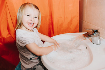 Cute little toddler girl washing her hands in a bathroom. Hygiene concept showing prevention of infection and viruses such as flu and covid-19