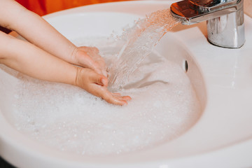Fototapeta premium Cute little toddler girl washing her hands in a bathroom. Hygiene concept showing prevention of infection and viruses such as flu and covid-19