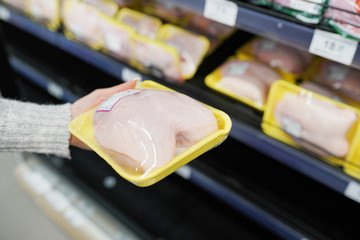 Woman choosing packed chicken meat in supermarket