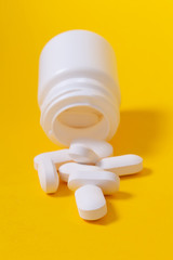 White pills falling from plastic medicine jar.