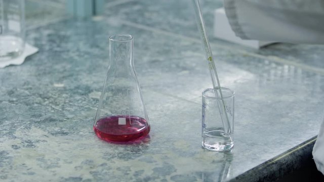 operator takes a sample of water or solution in a measuring tube in front of a chemical indicator flask close up medical industry