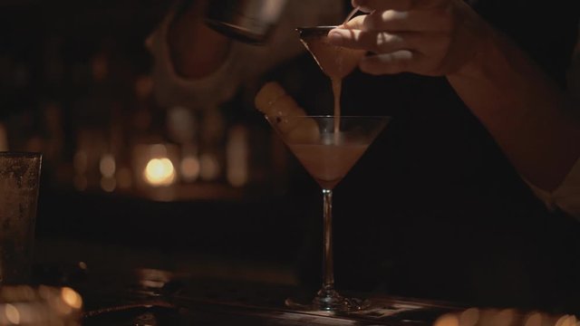 Real time close up shot of a bartender pouring a cocktail into a glass. Bartender prepares cocktails at a bar in Bangkok, Thailand. Decoration of a cocktail.