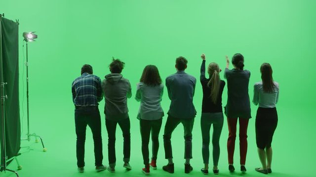 Green Screen Chroma Key Studio: Diverse Row of Seven Fans Cheering, Jumping and Applauding with Hands in the Air at the Public Sport Event, Concert, Festival, Party. Back View Full Shot. Slow Motion
