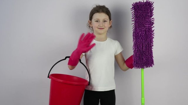 little girl with cleaning products, a MOP and a bucket waves a happy hand in greeting.