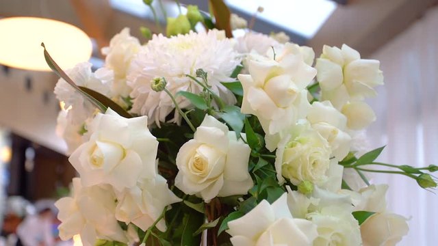 Close-up shooting of open and fresh white roses standing in a vase and prepared for a wedding party. Beautiful flowers adorn the wedding table in the hall for the celebration of the bride and groom.
