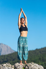 Girl practices yoga on top of the mountain.