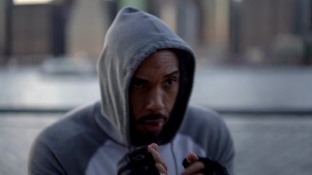 Slow motion effect of young African American sportsman in tracksuit boxing and doing exercises before cardio workout jumping at urban settings at metropolitan bund, concept of determinate for goal
